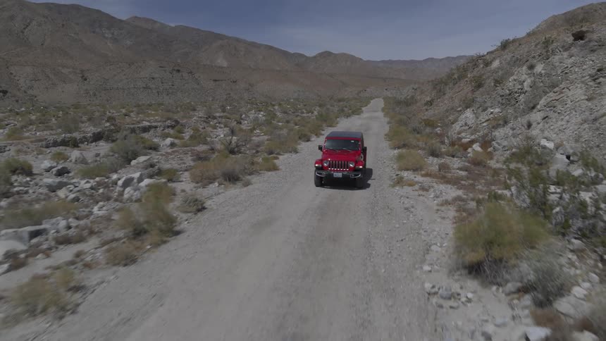 Red truck drives along road among badlands
