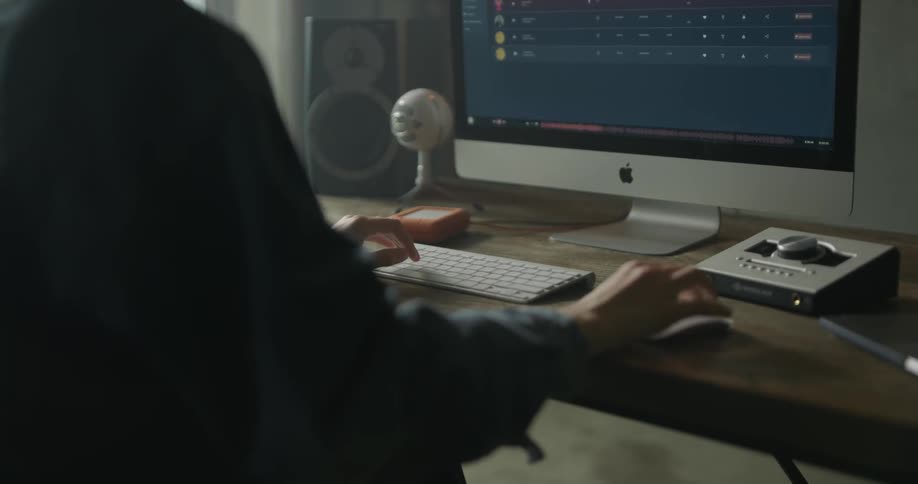 Woman types on white keyboard before large monitor
