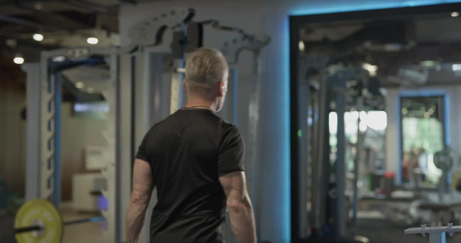 A man in a gym picks a dumbbell off a rack and carries it