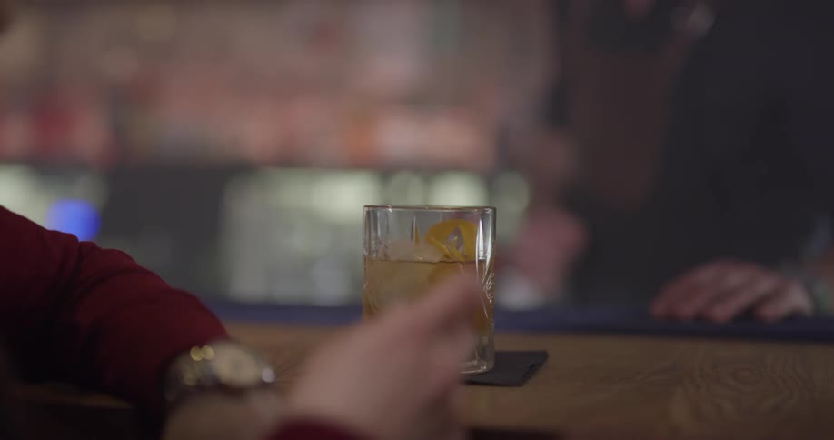 A bartender serves a cocktail to a person sitting at the bar