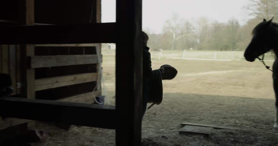 A woman is putting a saddle on a horse