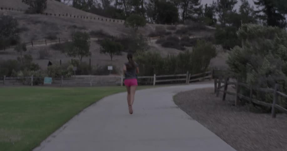 Woman runs along paved path in park during the day