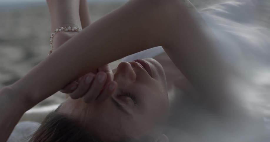Woman lying on the beach crosses her arms over her forehead