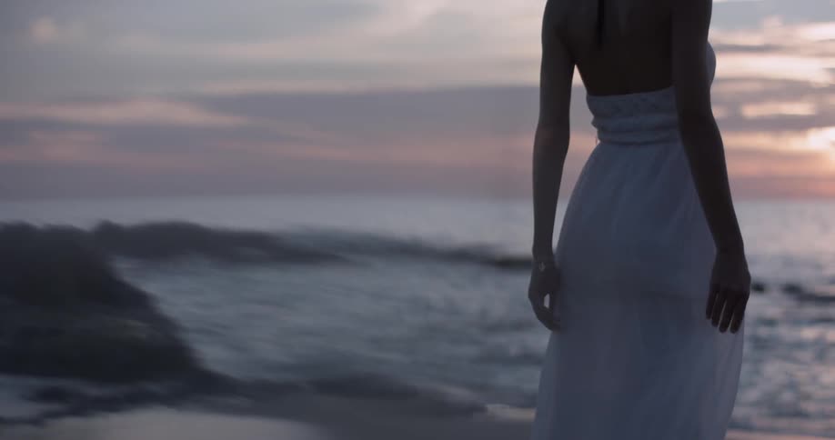 Woman stands on the beach looking out to the ocean