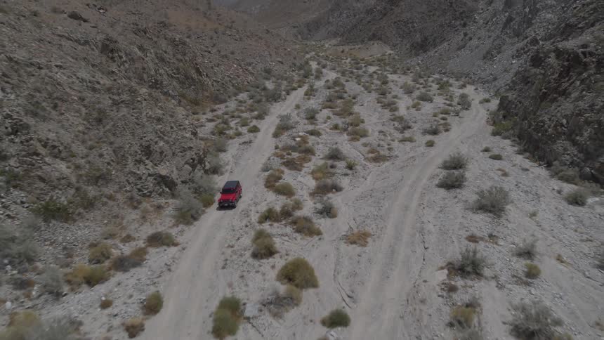 Red truck drives along road in arid valley between rocky hills
