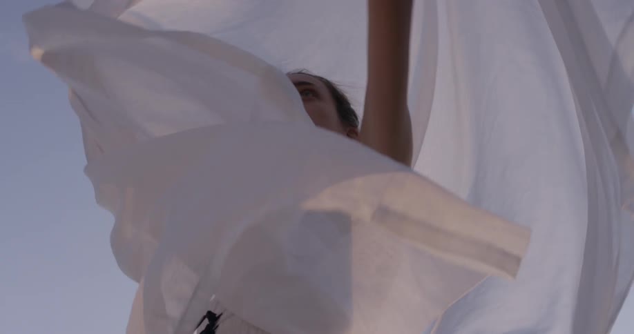 A woman twirls outside with a white sheet