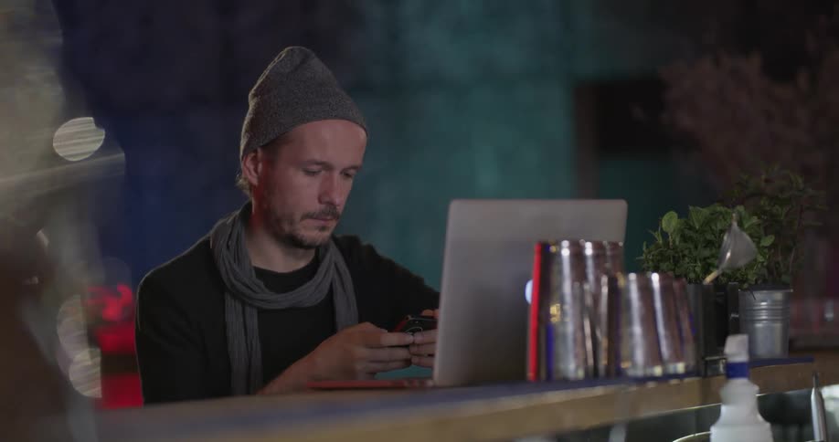 A man sitting with a laptop picks up his cell phone