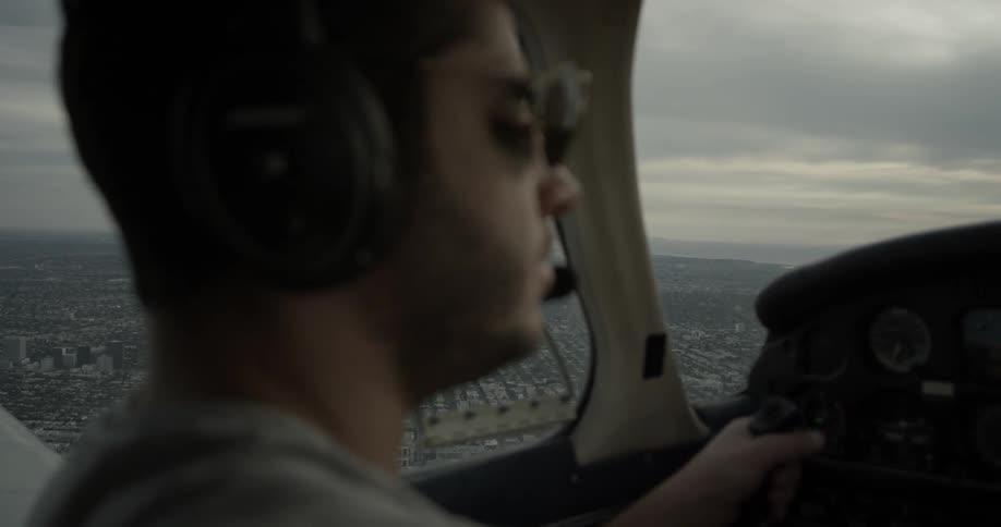 A pilot wearing aviators sits in the cockpit of a plane