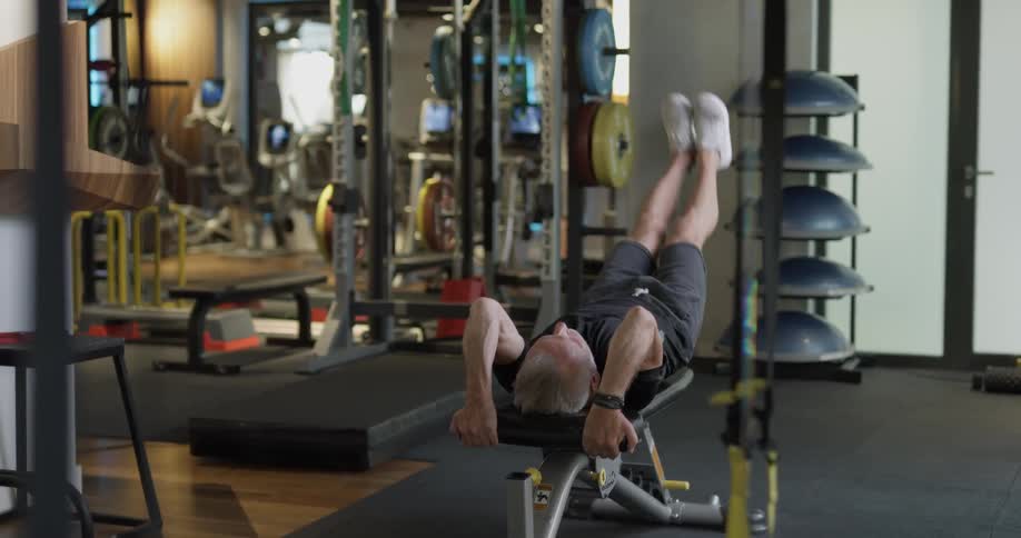 An elderly man does leg lifts on a workout bench