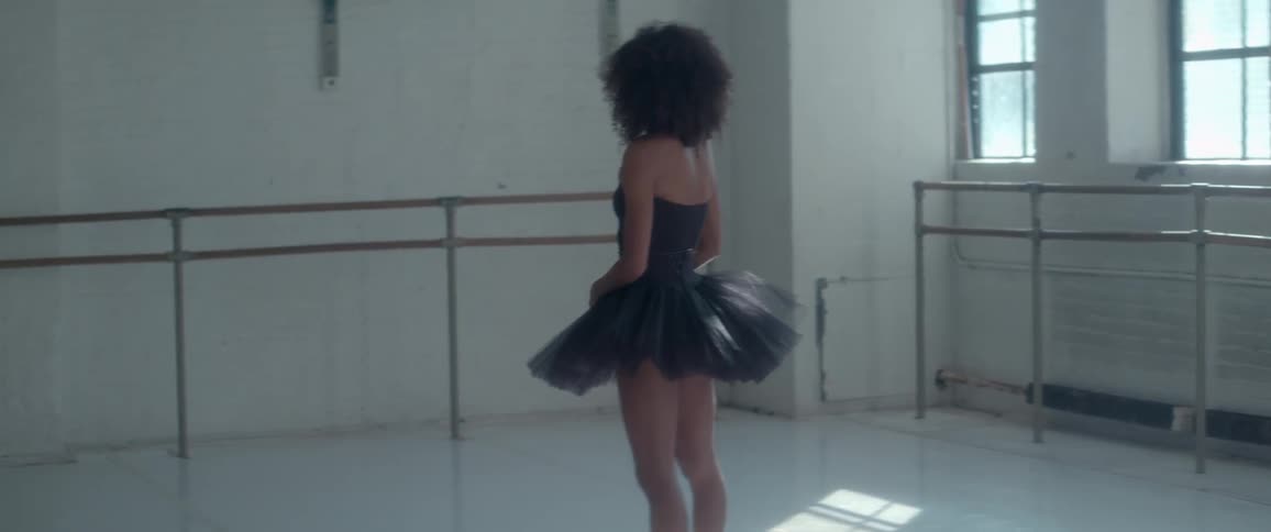 Woman in a black tutu stands in a ballet studio alone
