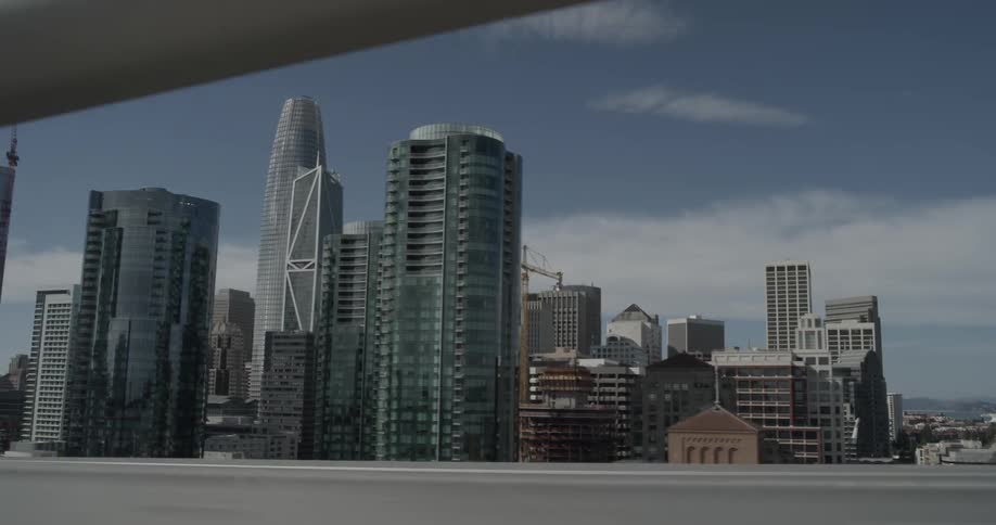 Car passes bridge supports while camera shows a large city in the background