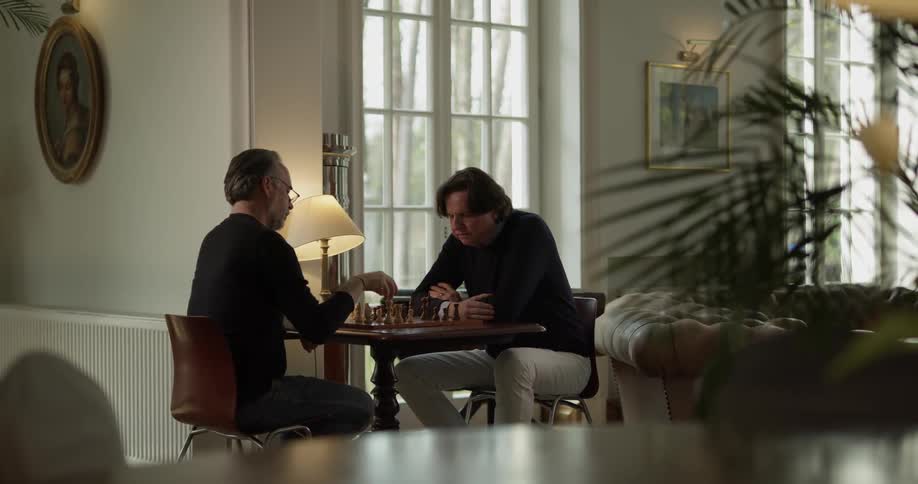 Two men sit in living room and play chess