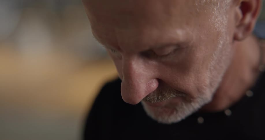 Camera circles around a man with a closeup of his face and his gray beard hair with black shirt and a blurry background