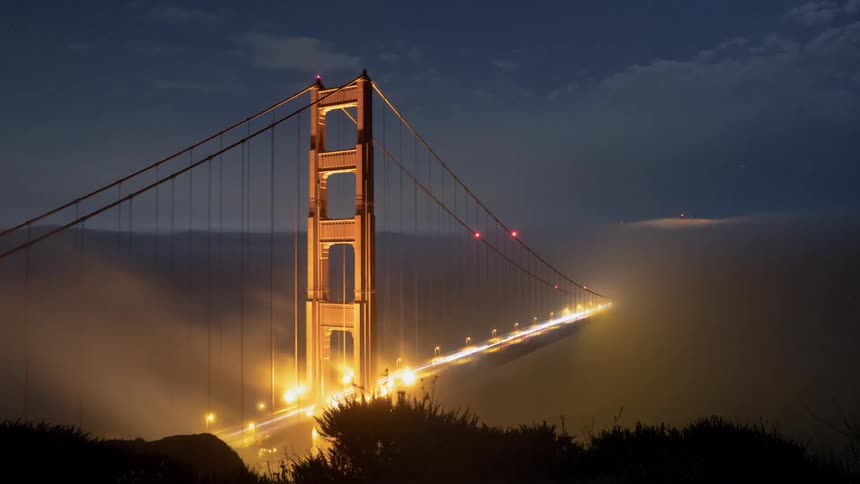 Bright lights from vehicles seen moving across a bridge