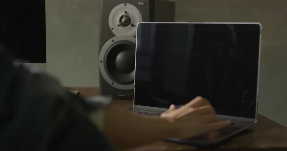 A woman is sitting at the computer desk with a computer mouse and laptop with large speakers and black screens on a sunny day
