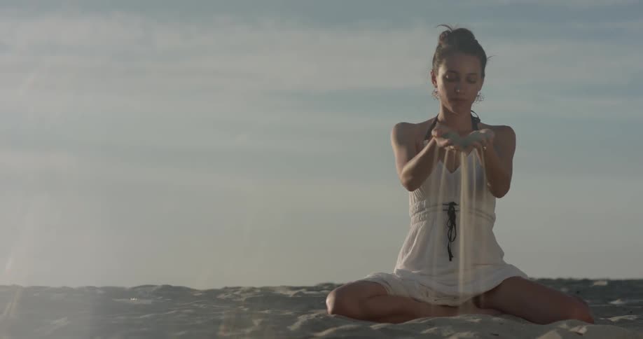 A woman drops sand from her hands on the beach