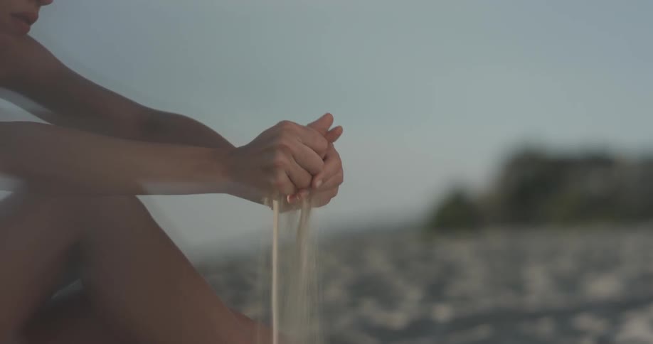 Woman sits on beach and sifts sand through her hands