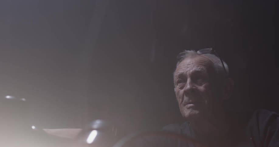 An old man sits illuminated by a single light to his right