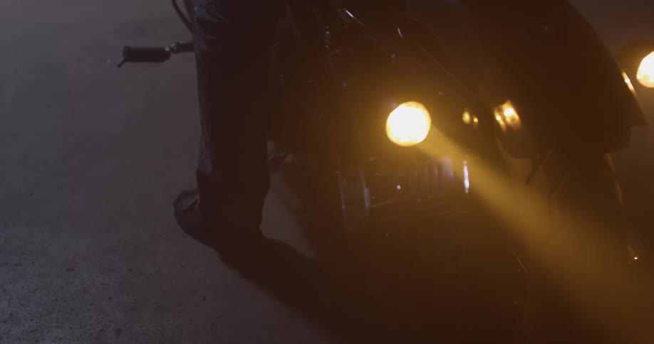 Man mounts motorcycle and turns it on at night