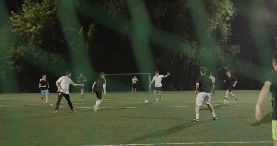 Two teams of men play soccer and one man kicks the ball into the net