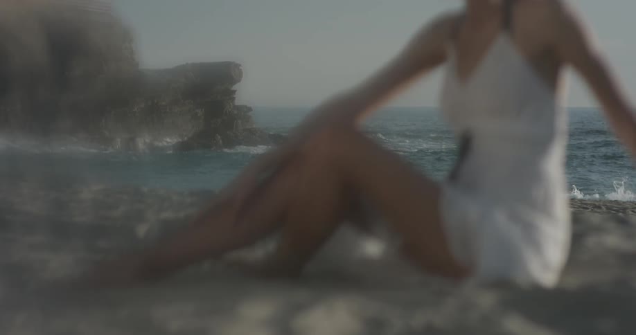 Woman in a white dress sits on the seashore and moves her hands along the ground