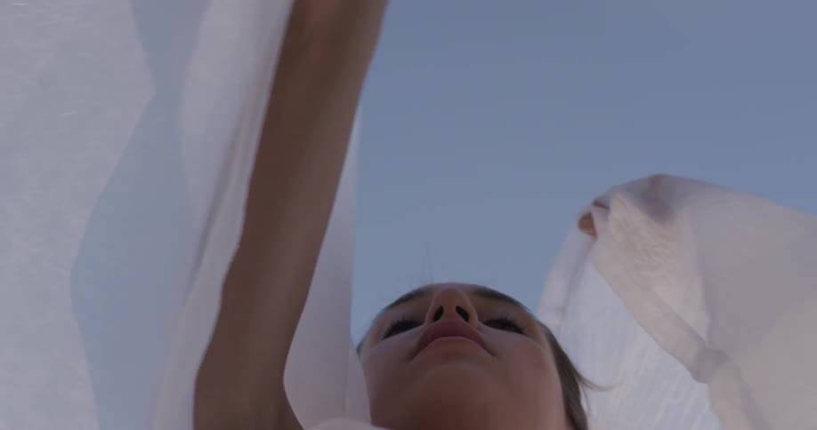 A woman holds a gauzy white scarf and waves it in the wind around her