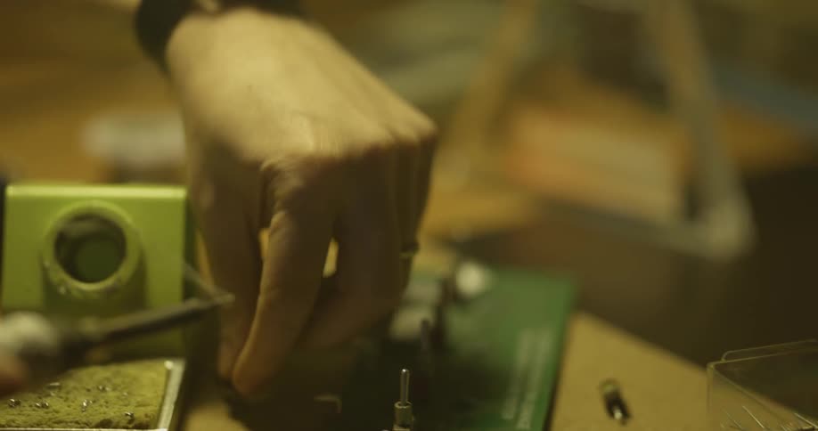 Hot smoke rises from a soldering pen and is moved to the circuit board for electronic music equipment