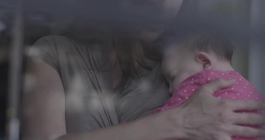 A woman holds a baby in front of a window