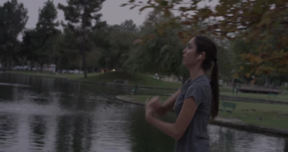 A woman stretches while walking alongside a pond