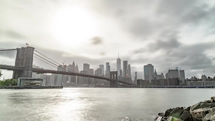 Clouds are passing over a bridge into a city during the daytime