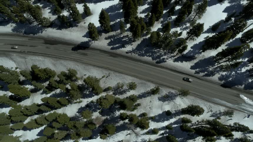 Cars drive in opposite directions along a curved road through a forest in the winter