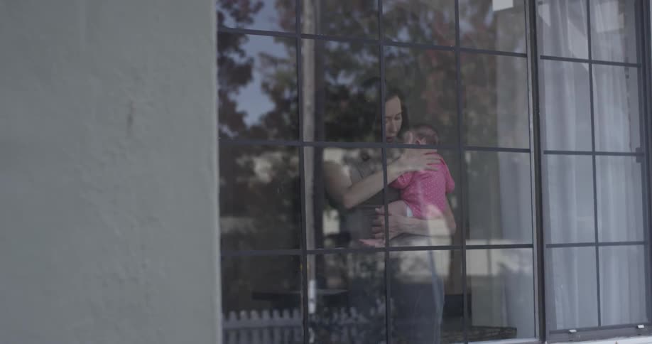 A woman holds a sleeping baby in front of a window