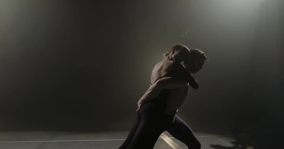 Man and woman performing dance while wearing tights in a dark room with a spotlight