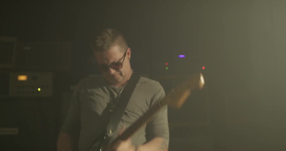 Man plays guitar indoors in dark room with a bright light