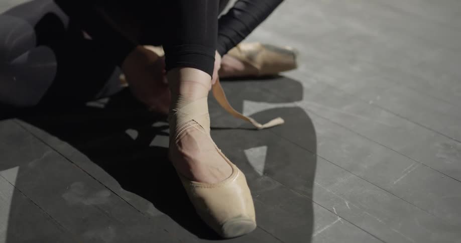 Woman wraps straps of a ballet shoe around her ankle