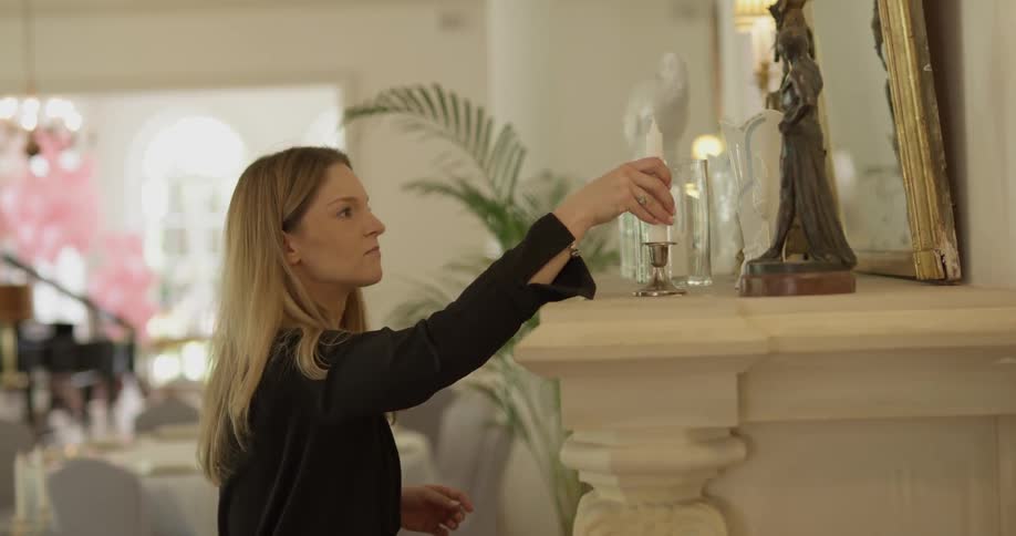 Woman is setting up candles on fireplace mantle