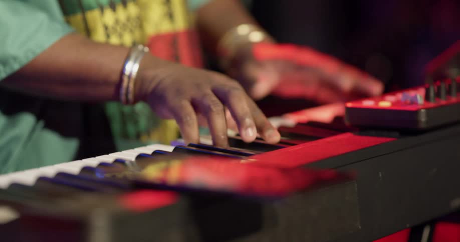 An African woman stands up on stage playing a piano for a concert in red and blue lighting