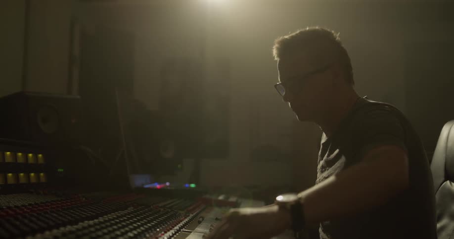 Man wearing glasses gestures and adjusts audio mixer