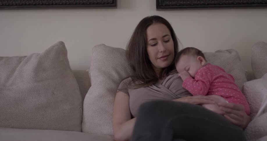 A woman sits with an infant sleeping on her shoulder