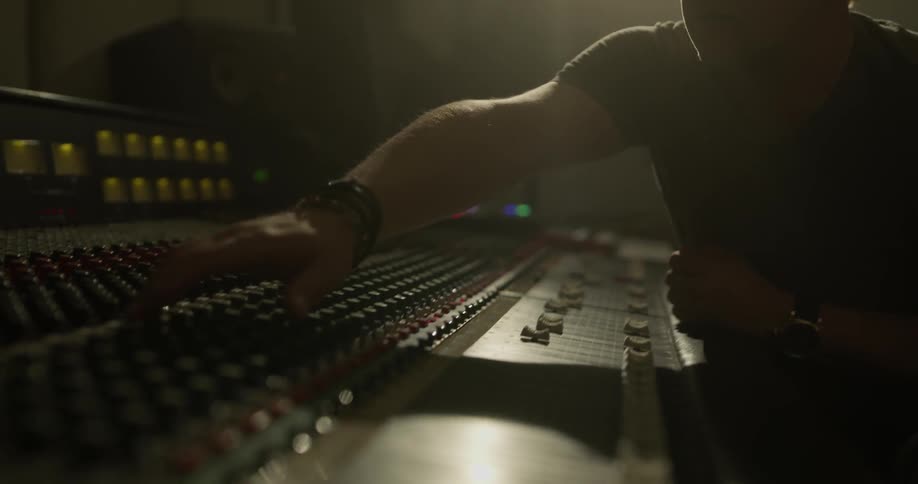 A man is nodding his head in time with a beat as he uses a a sound mixer in a studio