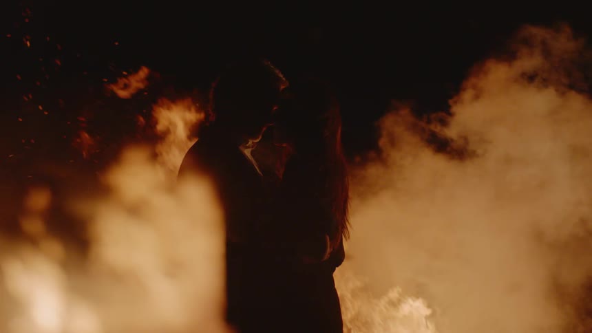 A man and woman kissing in front of a fire