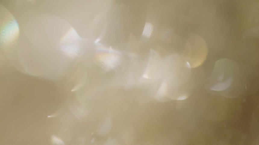 Shiny glass particles fall creating blurry lens flare rainbow effects in this abstract video with plenty of light