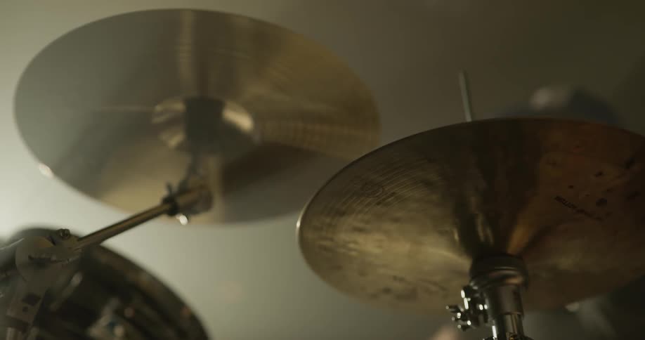 A man plays drums in a dark room with a bright light shining on him