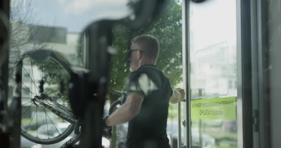 A man walking a bicycle out the door of a bike shop