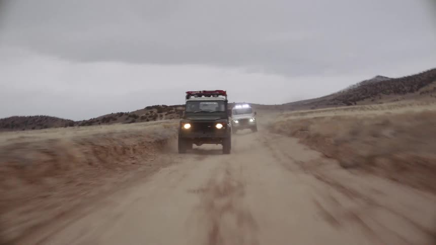 Two vehicles drive very fast along a rural dirt road