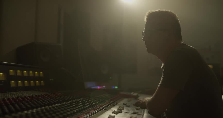 A man sits at a mixing board and adjusts the levels