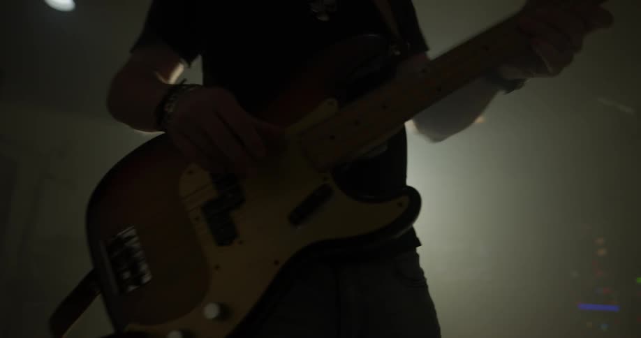 Man plays bass guitar in black room with bright light