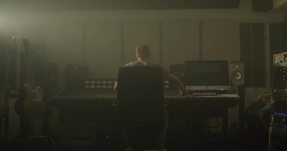 Man adjusts switches on a sound mixer among musical instruments