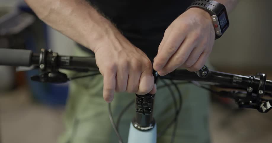 A man wearing a watch affixes a handle bar to a bicycle