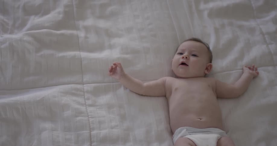 A baby moves its arms and legs while laying on a blanket